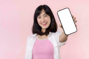 Lycklig leende ung asiatisk kvinna rekommenderar som visar ny Ansökan eller mobil annons, attrapp smartphone mall baner isolerat på rosa bakgrund. collage tom skärm digital mobil enhet. foto