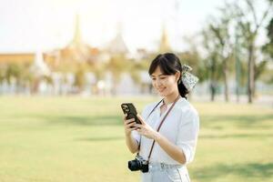 porträtt skön ung asiatisk kvinna med smartphone på sommar Semester semester resa med de stor palats i en bakgrund på Bangkok, thailand foto