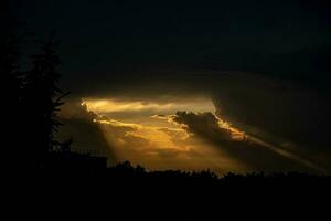 mörk tät himmel och strålar av värma orange ljus få ut av de moln foto