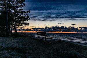 havet landskap med solnedgång och en ensam bänk stående på en dyn foto