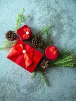 jul dekoration sammansättning på grå betong bakgrund med en skön röd gåva låda med röd band, träd grenar, och tall koner foto