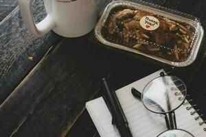banan kaka på en svart trä- tabell med notera bok, glasögon, och kaffe muggar. foto