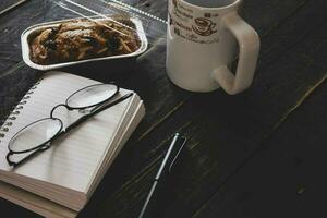 banan kaka på en svart trä- tabell med notera bok, glasögon, och kaffe muggar. foto
