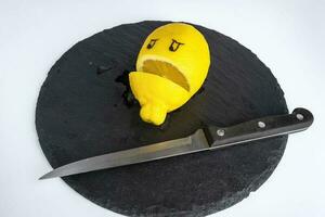 en kök kniv och en citron- med målad ögon skära i halv lögner på en skärande styrelse foto