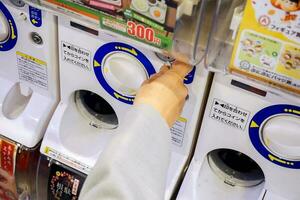 Osaka, Japan, 2018 -hand av turist innehav valuta mynt köp av en gashapong försäljning maskin i japan leksaker affär. gashapong är försäljning maskin dispenseras kapsel leksaker populär i japan. foto