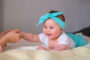 en 6 månader gammal bebis lögner på hans mage på de säng och finputsning hans systerns hand. en skön pannband för en bebis. foto