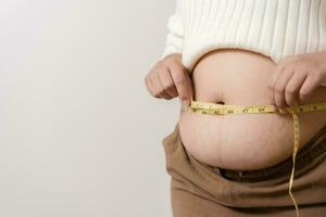 ett fetma använder sig av mätning tejp till visa de verklig storlek. knubbig fett kvinna använder sig av mäta tejp på mage. verklig storlek kvinna efter gav födelse till bebis, verklig hud med rynkor och ärr. foto
