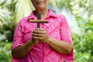 närbild senior kvinna innehar trä- korsa utomhus. begrepp , kristen dyrkan. tro, förlåtelse, tro, kärlek och hoppas. religiös symbol av kristendomen. foto