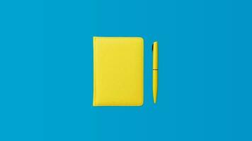 Foto av stängd gul anteckningsbok och kulpenna penna över blå bakgrund. minimalistisk bild av stängd dagbok och gul penna som tillbaka till skola begrepp.