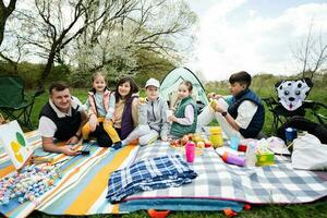 Lycklig ung stor familj med fyra barn har roligt och njuter utomhus- på picknick filt på trädgård vår parkera, avslappning. foto