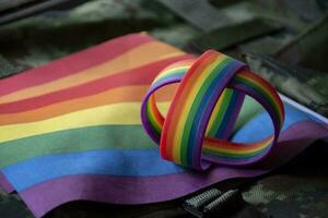 regnbåge flagga och regnbåge armband på kamouflage bakgrund, begrepp för fester av HBTQ människor i stolthet månad runt om de värld, mjuk och selektiv fokus på armband. foto