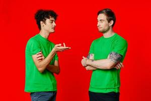 två vänner i grön t-tröjor är stående sida förbi sida kommunikation positiv röd bakgrund foto