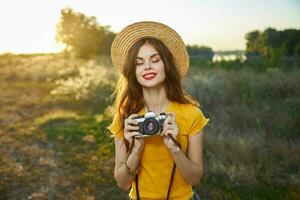 kvinna med stängd ögon med en kamera i henne händer bär en hatt röd mun natur Sol livsstil foto