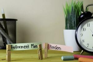 pensionering planen och pension. handstil på klibbig anteckningar i kläder pinnar på trä- kontor skrivbord foto