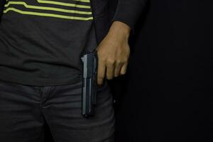 asiatisk man innehar en pistol. pistol i hans hand isolerat på svart bakgrund. foto