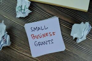 begrepp av små företag bidrag skriva på klibbig anteckningar isolerat på trä- tabell. foto