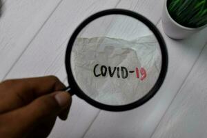 covid-19 skriva på knäckt papper med förstorande glas isolerat på trä- tabell. foto