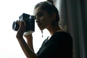 skön kvinna innehav en kamera nära de fönster dekoration mode livsstil studio foto