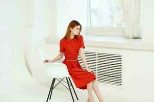 skön kvinna i röd klänning Sammanträde på en stol elegant stil foto