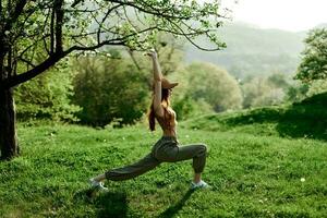 en ung atletisk kvinna gör sporter stretching i natur i de parkera. grön sommar landskap i de solljus i natur foto
