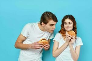 ung par hamburgare i händer mellanmål livsstil blå bakgrund foto