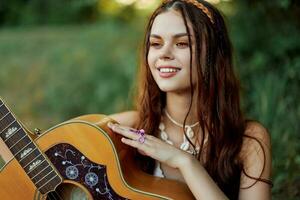 ung hippie kvinna med eco bild leende och ser in i de kamera med gitarr i hand i natur på en resa foto