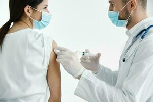läkare i vit täcka injicering en kvinnas axel vaccination skyddande handskar kvinna patient i de sjukhus foto