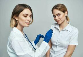 Lycklig kvinna läkare i blå handskar och kvinna patient i vit t-shirt stetoskop medicinsk klänning foto