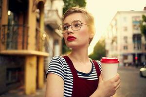 Söt kvinna med glasögon på de gata promenad en kopp av kaffe foto