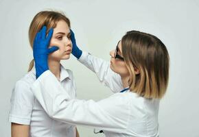en kvinna läkare i en medicinsk klänning och blå handskar undersöker de patientens ansikte foto