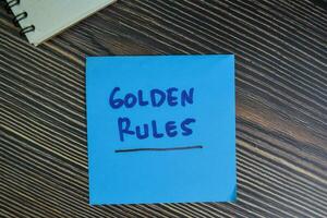 gyllene regler skriva på klibbig anteckningar isolerat på trä- tabell. foto