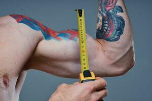 söt idrottare med centimeter tejp kondition modell kroppsbyggare tatuering på hans ärm grå bakgrund foto