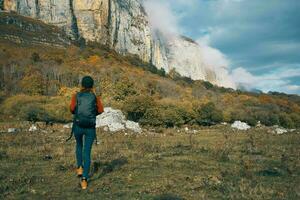 kvinna i jeans stövlar och en Tröja med en ryggsäck är vilar i de höst i de bergen i natur foto