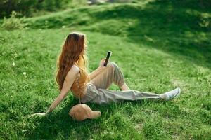 frilans studerande arbetssätt på de telefon Sammanträde utomhus i de sommar på grön gräs, mobil och internet ut av stad foto