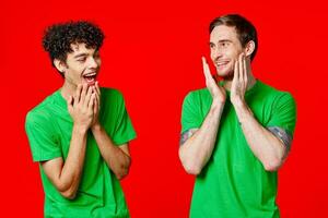 två män innehav deras huvuden i grön t-tröjor på en röd bakgrund foto