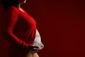 närbild gravid kvinna, förväntans mor Framställ bar mage med en vit ellerbarn blomma, på isolerat röd bakgrund. foto