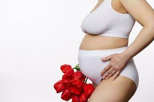 närbild gravid kvinna, förväntans mor i vit underkläder, Framställ med en bukett av röd tulpaner, på vit bakgrund foto