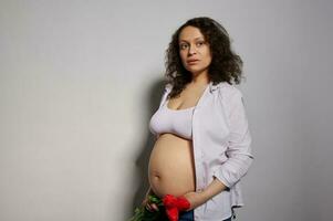 attraktiv sexig afrikansk amerikan gravid kvinna med röd tulpaner på mage. graviditet 24 Veckor. 6 månad. moderskap begrepp foto