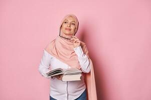 fundersam muslim gravid kvinna i hijab, innehav bok drömmande ser bort, resonemang på henne planer medan moderskap lämna foto