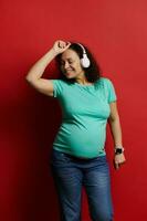 vuxen gravid kvinna dans lyssnande till musik på hörlurar, njuter underbar stunder av Lycklig sorglös graviditet foto