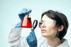 kvinna laboratorium assistent ser genom en förstorande glas på en kemisk lösning analys diagnostik foto