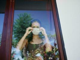 kvinna i medicinsk mask ser ut de fönster foto
