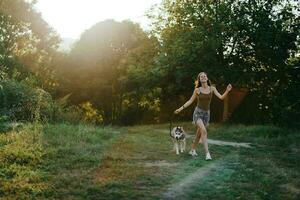 en kvinna kör med en hund i de skog under ett kväll promenad i de skog på solnedgång i höst. livsstil sporter Träning med din älskad hund foto