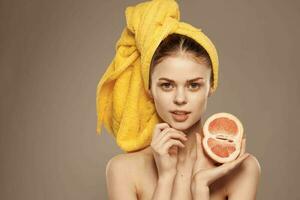 kvinna med bar axlar gul handduk på henne huvud grapefrukt i händer rena hud vård foto