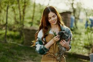 kvinna innehav en ung, friska kyckling och leende i natur på en bruka växande organisk, friska mat foto