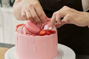 kvinna bakverk kock dekorerar rosa kaka med macaroons och bär, närbild. kaka framställning bearbeta, selektiv fokus foto