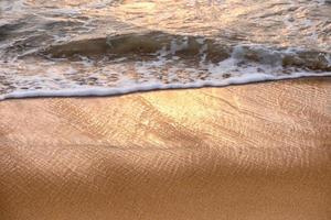 glänsande tropisk havsvåg med bubbla på brun strand vid solnedgången