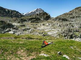 nöjd manlig turist efter klättrande lögner och vilar på de grön gräs mot de bakgrund av de berg. foto