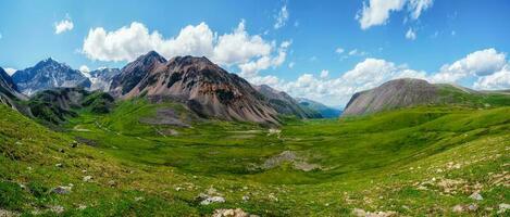 naturskön grön blå alpina panorama- landskap med högland dal i solljus och stor glaciär under blå molnig himmel. skugga av moln på grön berg dal foto