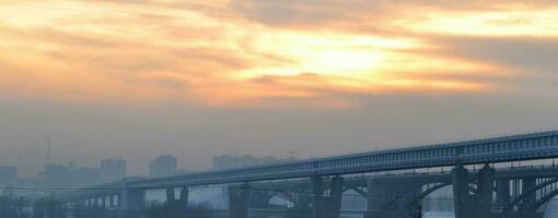 stad på skymning, stad byggnader mot de himmel, förorenad luft, fattig ekologi, järnväg bro foto